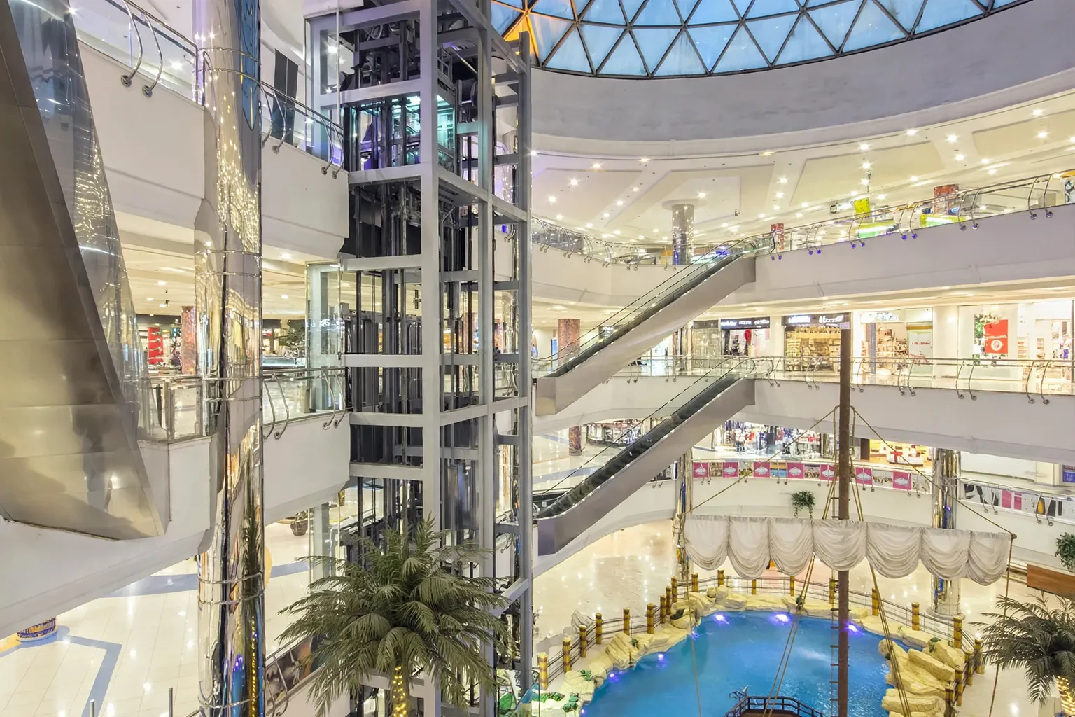 Atrium pusat perbelanjaan yang terang dan luas dengan atap kaca dan lantai marmer