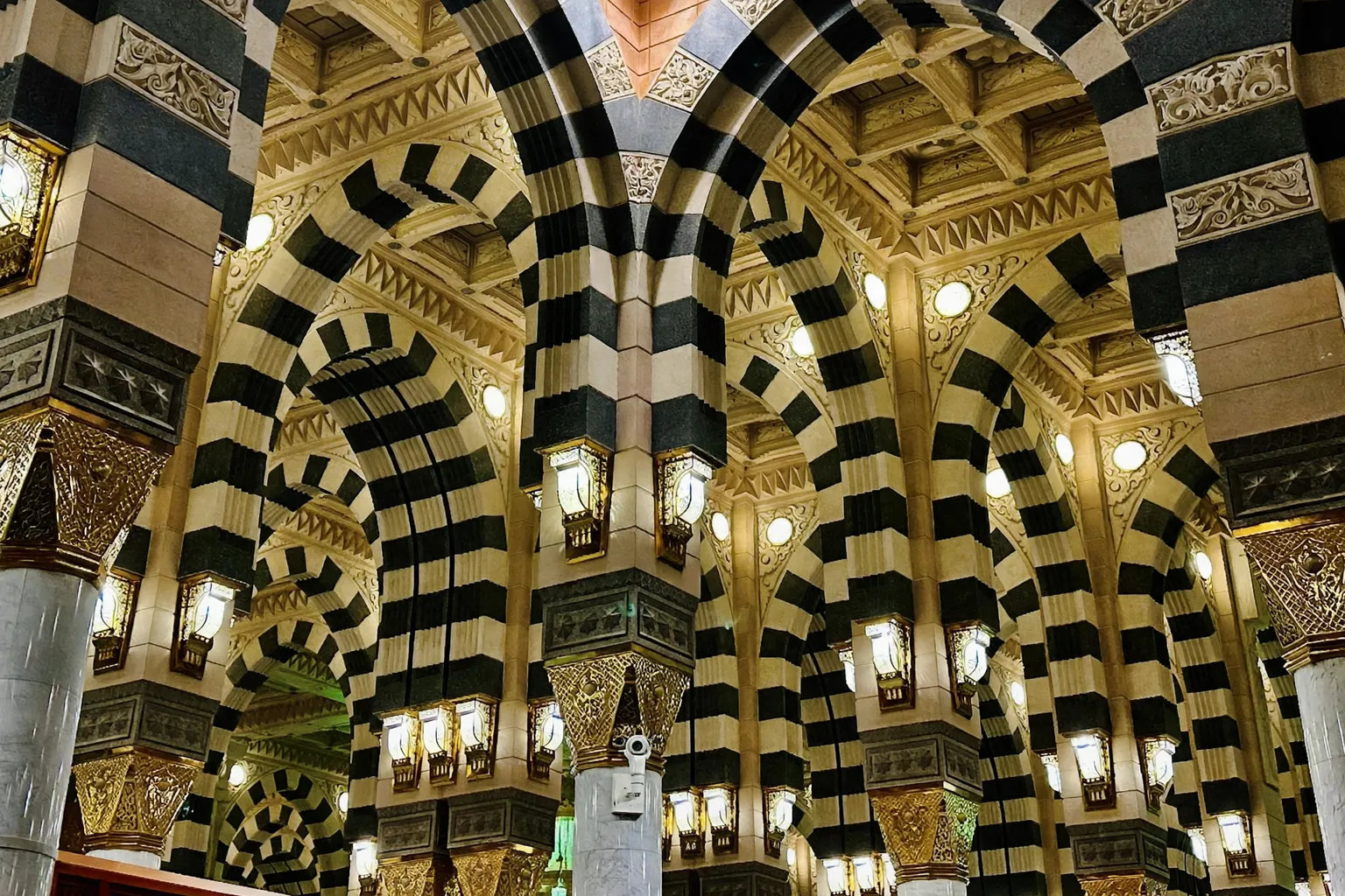 Lengkungan bergaris hitam putih dan kepala kolom bersepuh emas di dalam salah satu ruang salat Masjid an-Nabawi